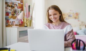 na zdjęciu uśmiechnięta uczennica pracująca na laptopie