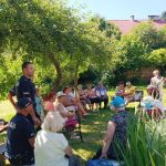na zdjęciu widoczni seniorzy oraz policjanci siedzący i rozmawiający w ogródku