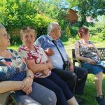 na zdjęciu widoczni seniorzy siedzący i rozmawiający w ogródku